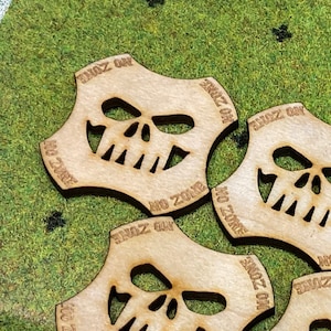 May include: Five wooden tokens with a skull design and the text "No Zone" around the edge. The tokens are light brown and have a slightly rough texture.