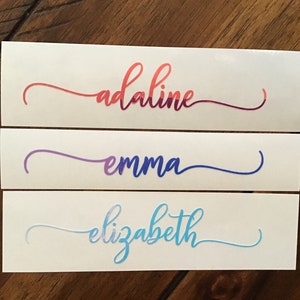 May include: Three white labels with names written in a cursive font. The names are "adaline" in red and purple, "emma" in purple and blue, and "elizabeth" in blue and light blue.