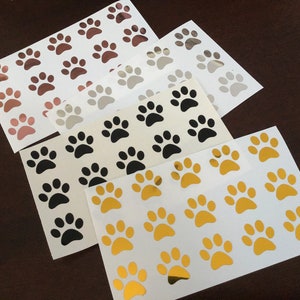 May include: Four sheets of paw print stickers in gold, black, silver, and rose gold. Each sheet has 16 paw prints.