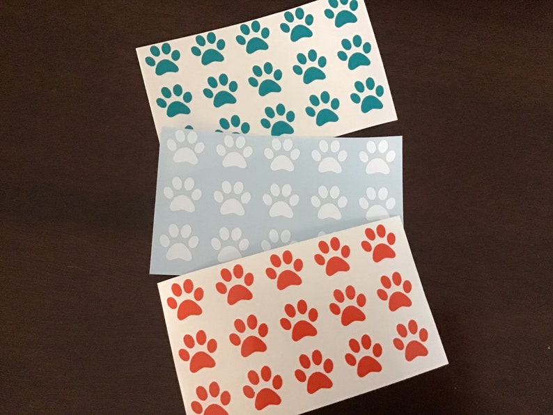 May include: Three sheets of white paper with paw prints in different colors. The top sheet has teal paw prints, the middle sheet has white paw prints, and the bottom sheet has orange paw prints.