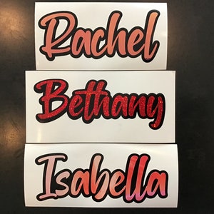 May include: Three white vinyl stickers with names written in cursive. The names are Rachel, Bethany, and Isabella. The names are written in different shades of red and pink with black outlines.