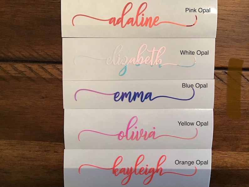 May include: Five vinyl stickers with different names written in cursive script. The names are Adaline, Elizabeth, Emma, Olivia, and Kayleigh. Each sticker has a different coloured background, including pink, white, blue, yellow, and orange.