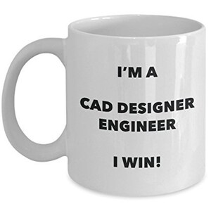 May include: White ceramic mug with a curved handle. The mug has the text "I'M A CAD DESIGNER ENGINEER I WIN!" printed in black, bold letters. The mug is designed for CAD designers and engineers.