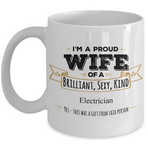 May include: White ceramic coffee mug with a black and gold design. The mug reads "I'm a proud wife of a brilliant, sexy, kind electrician. Yes - this was a gift from said person."