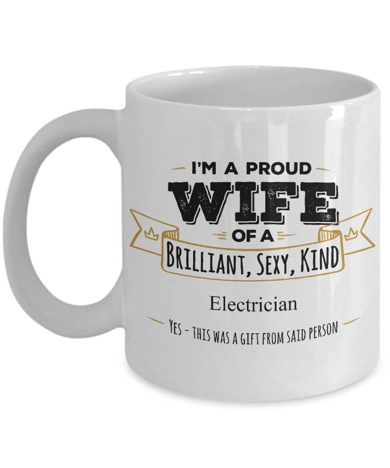 May include: White ceramic coffee mug with a black and gold design. The mug reads "I'm a proud wife of a brilliant, sexy, kind electrician. Yes - this was a gift from said person."