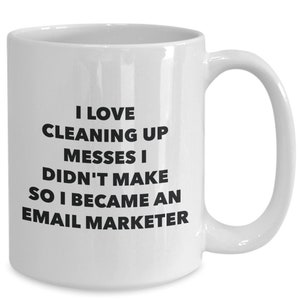 May include: White ceramic coffee mug with black text that reads "I love cleaning up messes I didn't make so I became an email marketer."