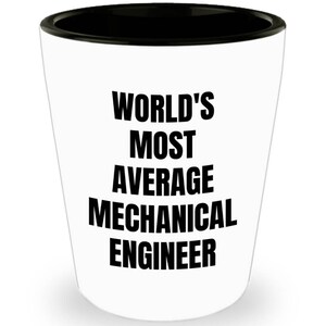 May include: White ceramic shot glass with a black rim. The glass has black text that reads "WORLD'S MOST AVERAGE MECHANICAL ENGINEER".