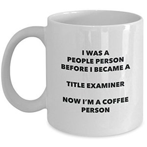 May include: White ceramic coffee mug with black text that reads "I was a people person before I became a title examiner. Now I'm a coffee person."