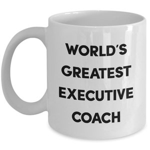 May include: White ceramic coffee mug with black text that reads "WORLD'S GREATEST EXECUTIVE COACH"