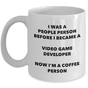May include: White ceramic coffee mug with black text that reads "I was a people person before I became a video game developer now I'm a coffee person."