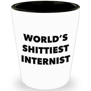 May include: White ceramic shot glass with a black rim. The glass has black text that reads "WORLD'S SHITTIEST INTERNIST".