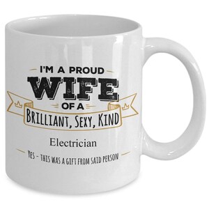 May include: White ceramic coffee mug with a black and gold design. The mug reads "I'm a proud wife of a brilliant, sexy, kind electrician. Yes - this was a gift from said person."