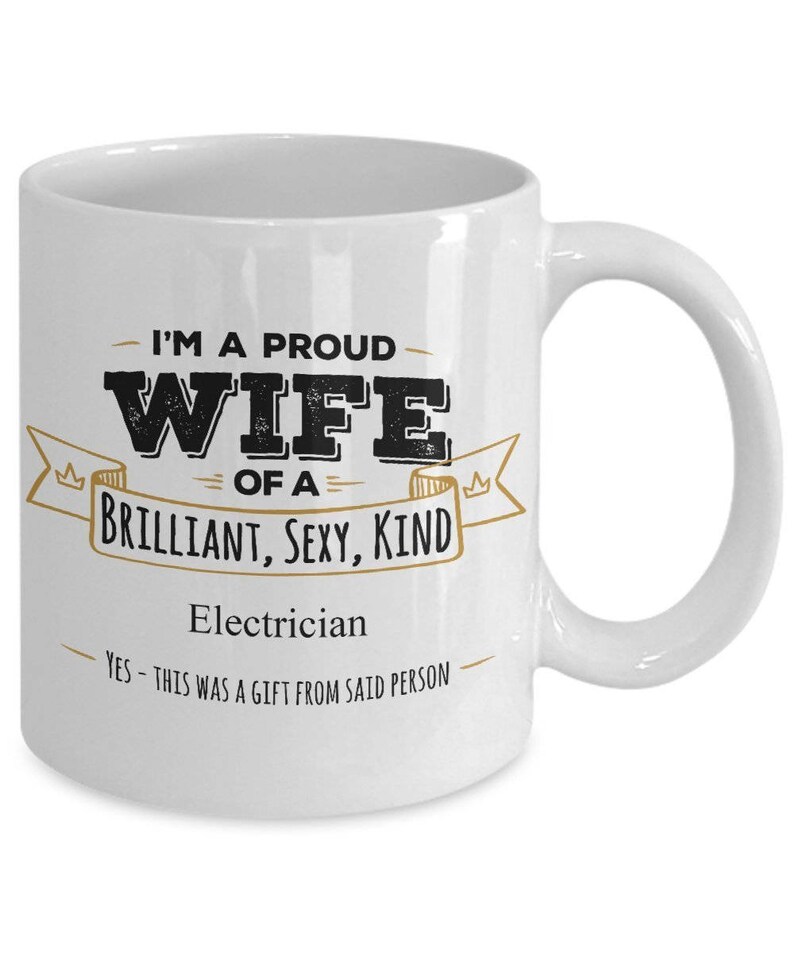 May include: White ceramic coffee mug with a black and gold design. The mug reads "I'm a proud wife of a brilliant, sexy, kind electrician. Yes - this was a gift from said person."