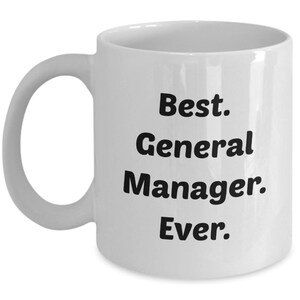 May include: White ceramic coffee mug with black text that reads "Best. General Manager. Ever."