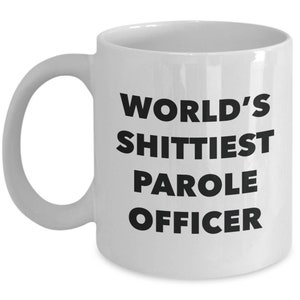 May include: White ceramic coffee mug with black text that reads "World's Shittiest Parole Officer".