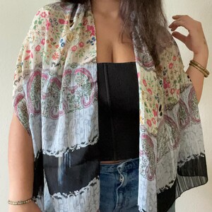 May include: A sheer, open-front kimono with a floral and paisley print in shades of pink, blue, and cream. The kimono has a black border and is made of a lightweight fabric, perfect for layering.