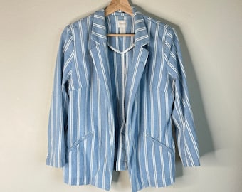 May include: A light blue and white striped blazer hanging on a wooden hanger. The blazer has a notched collar, two front pockets, and three-quarter length sleeves. The brand name "Chicos" is visible on the label.