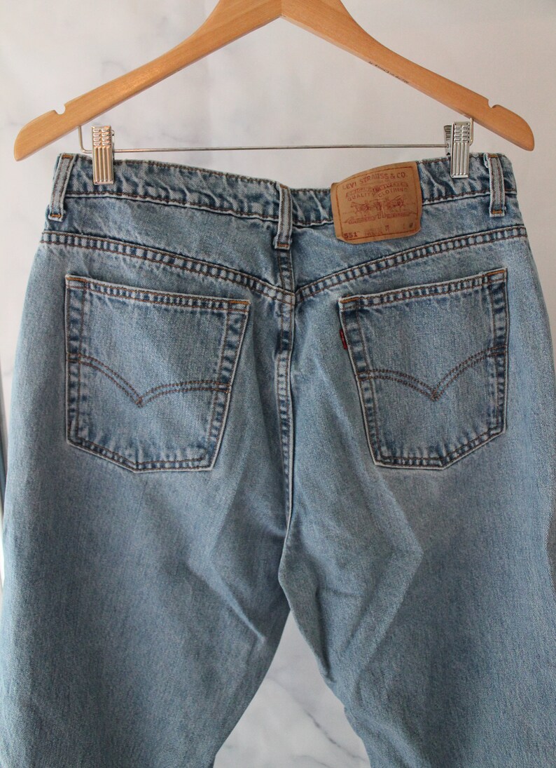 Puede incluir: Un par de pantalones vaqueros de mezclilla azul claro con un parche de la marca Levi's en el bolsillo trasero. Los pantalones tienen dos bolsillos traseros y cierre de bot&oacute;n.