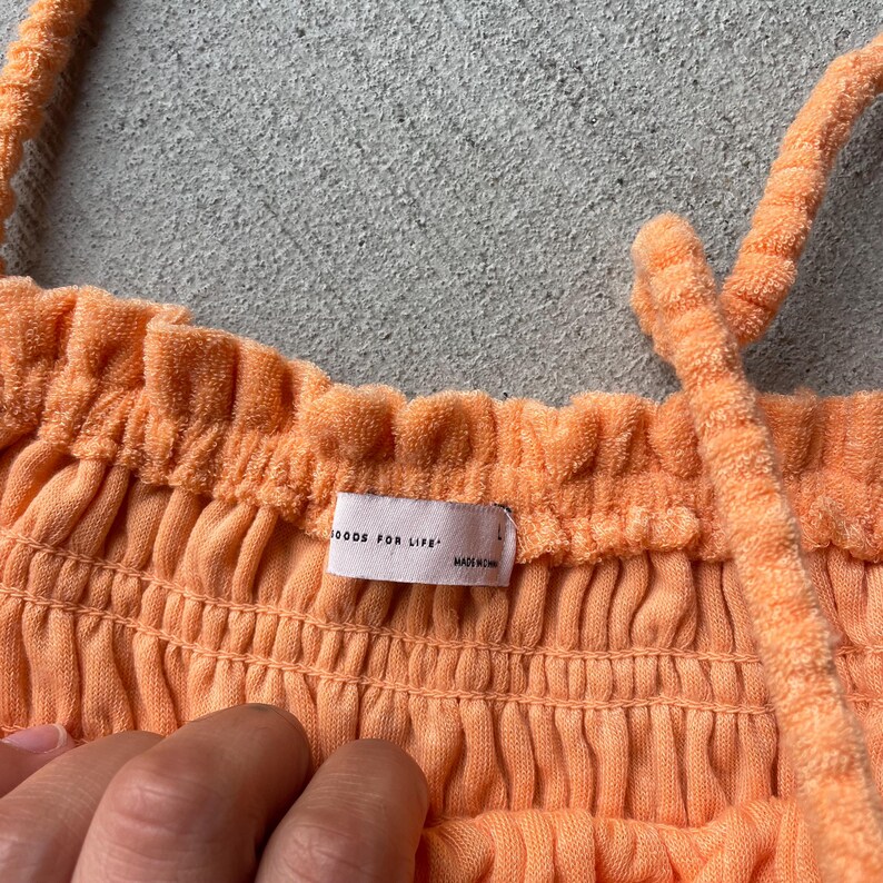 Pode incluir: Um top halter cor p&ecirc;ssego, canelado, com decote franzido e uma pequena etiqueta que diz "GOODS FOR LIFE" e "MADE IN CHINA".