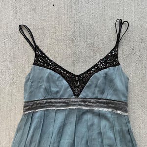 K&ouml;nnte beinhalten: Ein hellblaues, &auml;rmelloses Kleid mit einem schwarzen, perlenbesetzten Ausschnitt und einem grauen Samtbund.