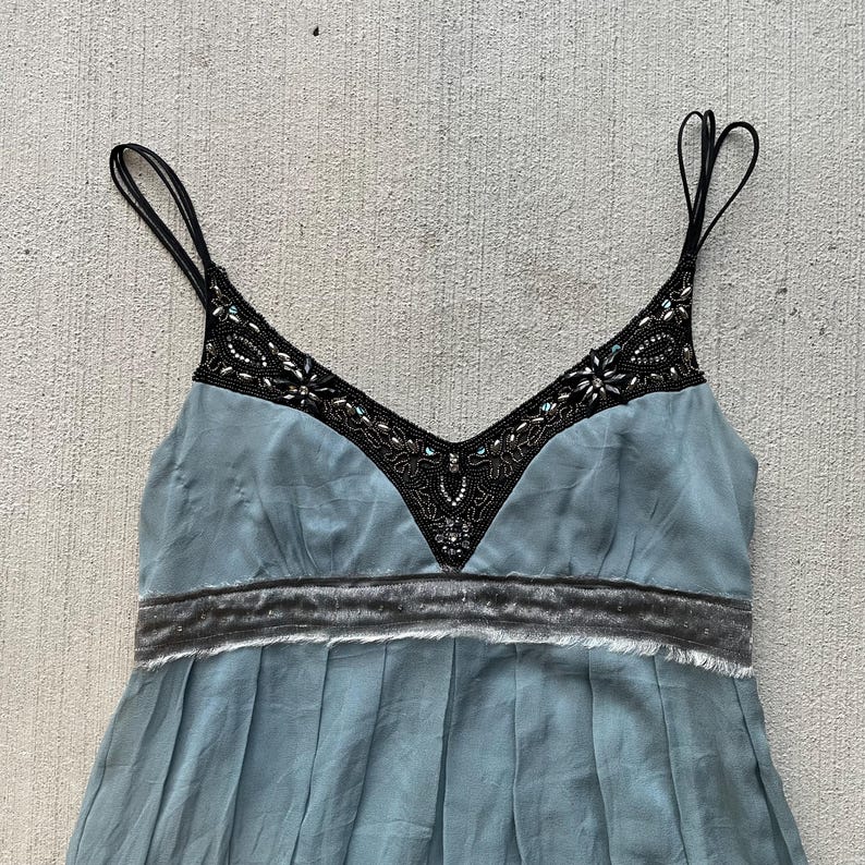 K&ouml;nnte beinhalten: Ein hellblaues, &auml;rmelloses Kleid mit einem schwarzen, perlenbesetzten Ausschnitt und einem grauen Samtbund.