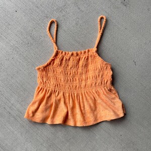 Pode incluir: Um top laranja brilhante sem mangas, franzido com uma bainha com babados.