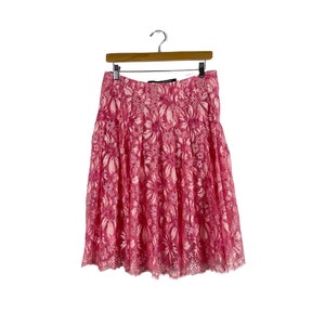 May include: A pink lace skirt with a floral pattern. The skirt is pleated and has a scalloped hem.
