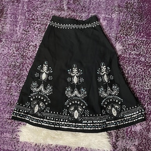 May include: A black A-line skirt featuring a waistband adorned with silver studs. The lower portion of the skirt is decorated with intricate vertical patterns of silver sequins, beads, and small light blue accents, finished with a wide beaded hem.