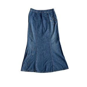 May include: A long, flared denim skirt in a medium wash blue. The skirt features vertical seams and decorative embellishments near the hem and pocket area. The skirt has a classic, timeless design.