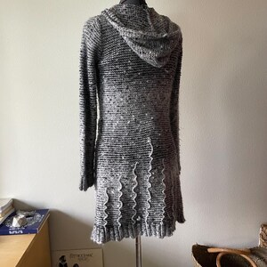 Puede incluir: Vestido de punto con capucha gris y negro con mangas largas, expuesto en un maniqu&iacute;. El vestido presenta un patr&oacute;n de punto texturizado, una capucha y un dobladillo con volantes. El vestido llega aproximadamente a la rodilla.