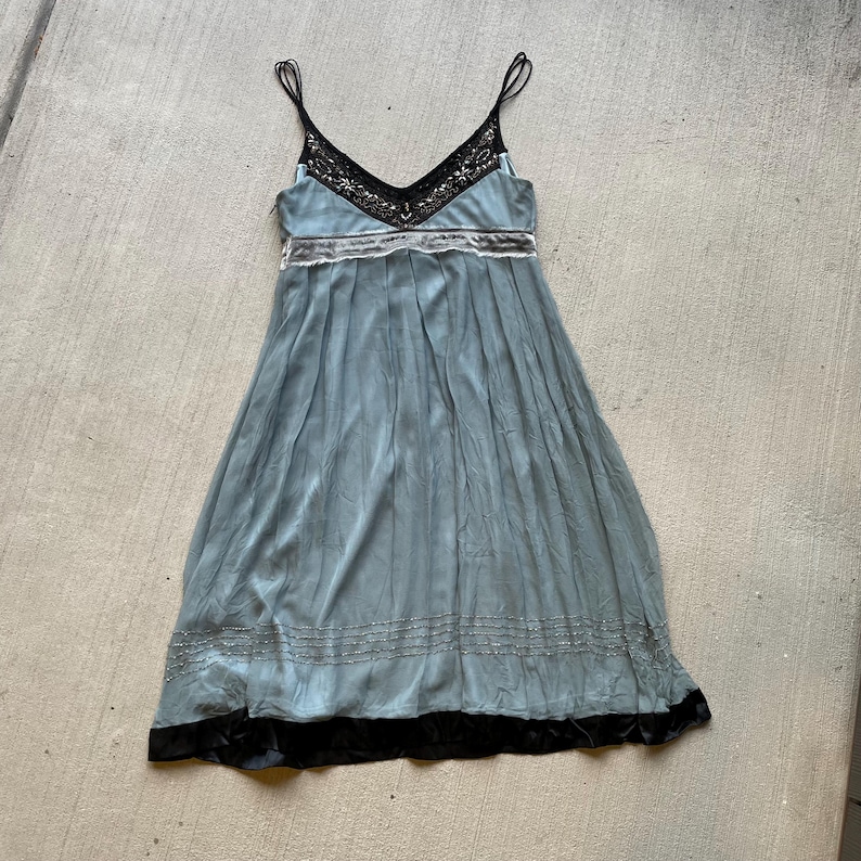K&ouml;nnte beinhalten: Ein hellblaues Maxikleid mit schwarzer Spitzenborte am Ausschnitt und schwarzem Samtbesatz am Saum. Das Kleid hat ein figurbetontes Oberteil und einen flie&szlig;enden Rock.