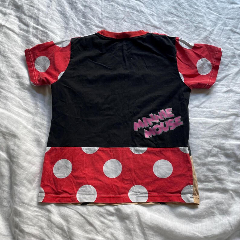 May include: A black and red t-shirt with a Minnie Mouse design. The top section is black, with the words "Minnie Mouse" in pink. The sleeves and lower section are red with white polka dots. The t-shirt has a round neck.