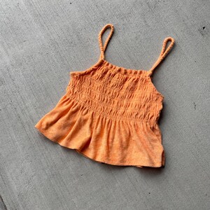 Pode incluir: Um top laranja brilhante sem mangas, com babados e um corpete franzido. O top &eacute; feito de um tecido macio e texturizado.