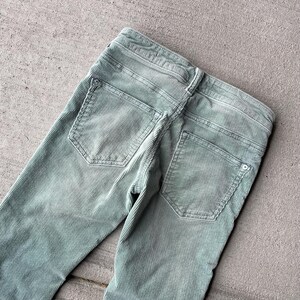 May include: A pair of light green corduroy pants with two back pockets. The pants are made of a soft, comfortable fabric and have a relaxed fit.