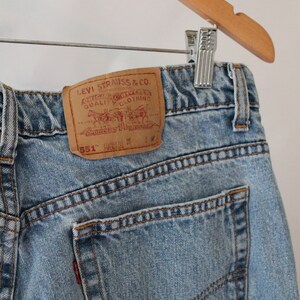 Puede incluir: Un par de pantalones vaqueros de mezclilla azul claro con un parche de cuero marr&oacute;n que dice "Levi Strauss & Co. Original Riveted Quality Clothing" y "551" en texto blanco.