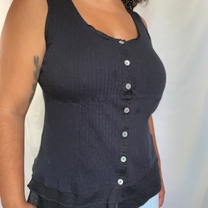 May include: A black sleeveless top with a button-up front and a layered ruffle hem.