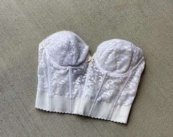 Puede incluir: Bustier de encaje blanco con escote de corazón y tirantes ajustables. El bustier tiene un corpiño con varillas y cierre de gancho y ojo en la espalda.