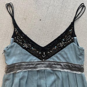K&ouml;nnte beinhalten: Ein hellblaues, &auml;rmelloses Kleid mit einem schwarzen Spitzen- und Perlenbesatz am Ausschnitt und einem grauen Samtbund.