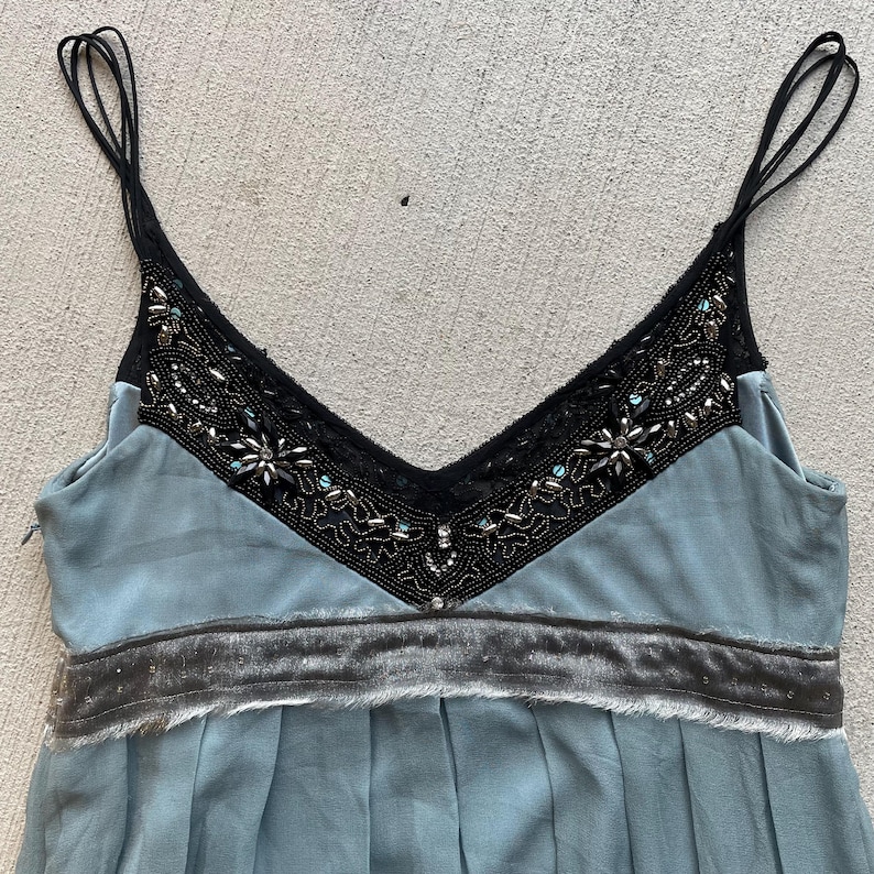 K&ouml;nnte beinhalten: Ein hellblaues, &auml;rmelloses Kleid mit einem schwarzen Spitzen- und Perlenbesatz am Ausschnitt und einem grauen Samtbund.