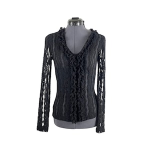 Pode incluir: Blusa preta de manga comprida transparente com decote de babados e silhueta ajustada.