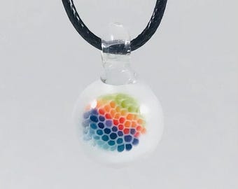 May include: A clear glass pendant with a rainbow-colored honeycomb design. The pendant is suspended from a black cord. The colorful design includes shades of red, orange, yellow, green, blue, and purple.