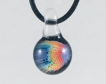 May include: A clear glass pendant with a colorful, abstract design. The pendant features a spherical shape with a rainbow of colors, including blue, orange, and yellow. It hangs from a black cord.