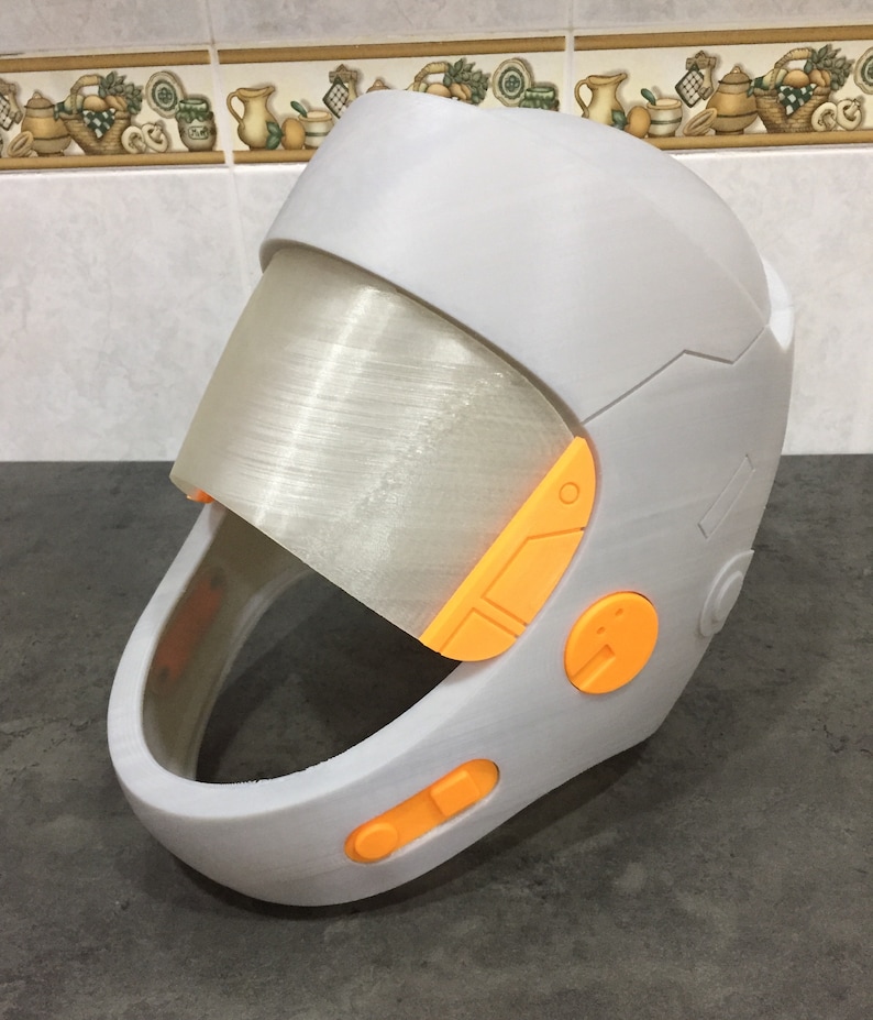May include: A white helmet with an orange visor and orange buttons. The helmet has a futuristic design.