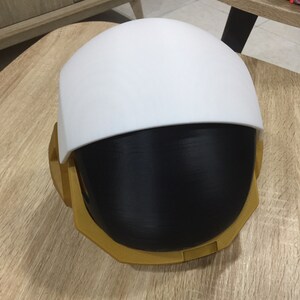 May include: A white and black helmet with a gold trim. The helmet has a rounded top and a flat bottom.