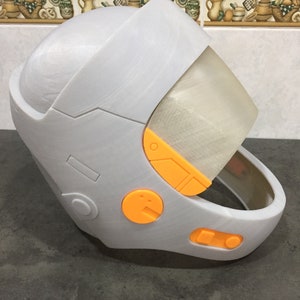 May include: A white helmet with orange accents and a clear visor. The helmet has a rounded top and a chin strap.