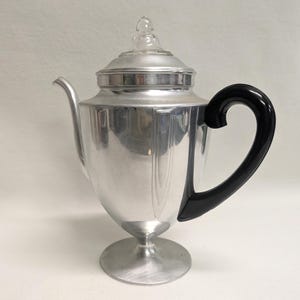 May include: Silver percolator coffee pot with a black plastic handle and a glass lid.