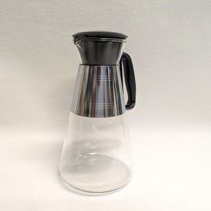 May include: A clear glass pitcher with a silver band around the middle and a black lid and handle.