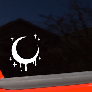 May include: White vinyl decal showing a crescent moon with dripping edges and stars. This celestial-themed graphic is a simple, yet striking design, suitable for decorating a car window or other smooth surface.