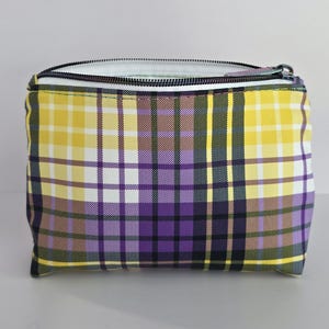 May include: A rectangular zippered pouch with a plaid pattern in yellow, purple, white, and black. The zipper is black with a silver pull. The interior lining is white.