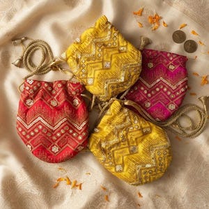 May include: Four drawstring pouches in red, magenta, and two shades of yellow, each featuring intricate gold embroidery, sequins, and a chevron pattern. The bags include gold braided cords with metallic tassels for closure and decorative accents.